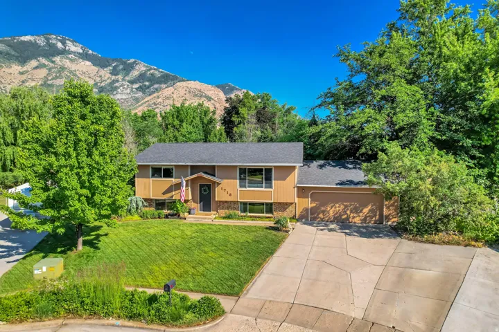 Split-level residence featuring a two-car garage, a well-maintained front lawn, and mature trees
