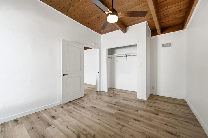 Wood-finish flooring with a vaulted wood-paneled ceiling, ceiling fan, and built-in closet with hanging rod