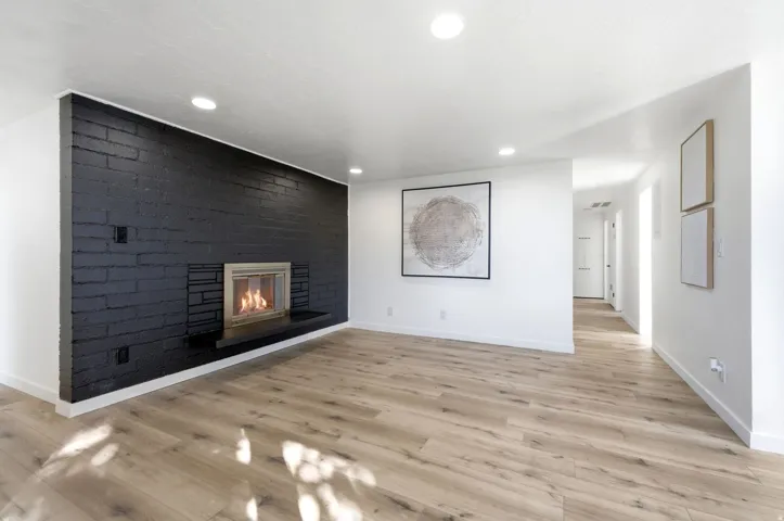 Accent brick fireplace with a raised hearth, wood-finish flooring, recessed lighting, and a neutral color palette