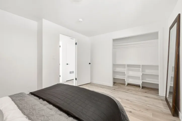Light wood-finish flooring, white walls, and an open closet with built-in shelving and hanging rods