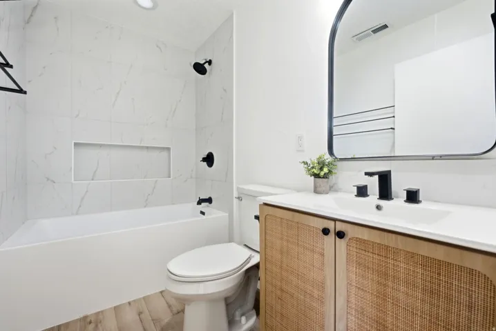 Bathroom featuring a white bathtub with a recessed niche, black fixtures, wood-finish flooring, a toilet, and a vanity with a white countertop