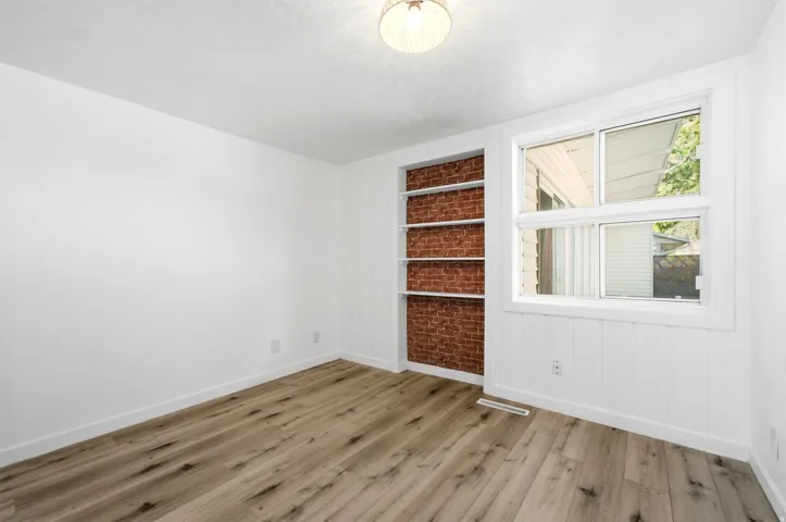 Bright corner room featuring wood-finish flooring, white walls, and large multi-pane window with natural light