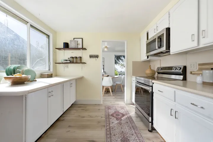 Kitchen with wood-finish flooring, white cabinetry, stainless steel appliances, and a window