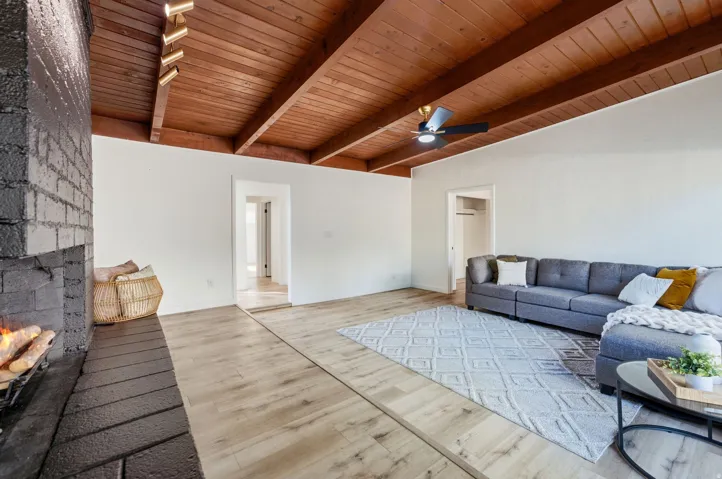Vaulted wood-paneled ceiling with exposed beams, wood-finish flooring, black brick fireplace, track lighting, and a ceiling fan