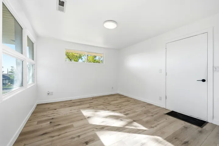 Bright and spacious room featuring pristine white walls, recessed ceiling lighting, and warm wood-finish flooring throughout