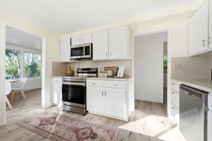 Kitchen featuring wood-finish flooring, white cabinetry, stainless steel appliances, and light-colored countertops