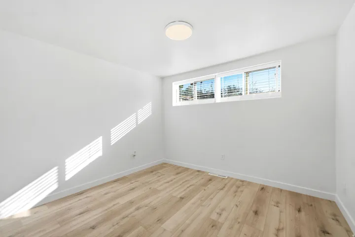 Recessed window with horizontal blinds, wood-finish flooring, white walls, and a ceiling-mounted light fixture