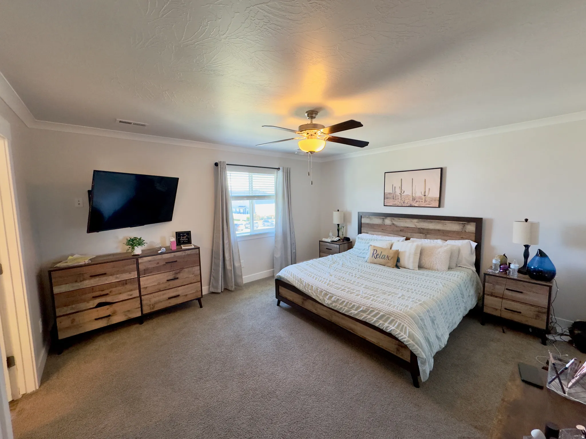Neutral-toned bedroom featuring carpet flooring, crown molding, a ceiling fan with integrated lighting, and a window with blinds and drapes