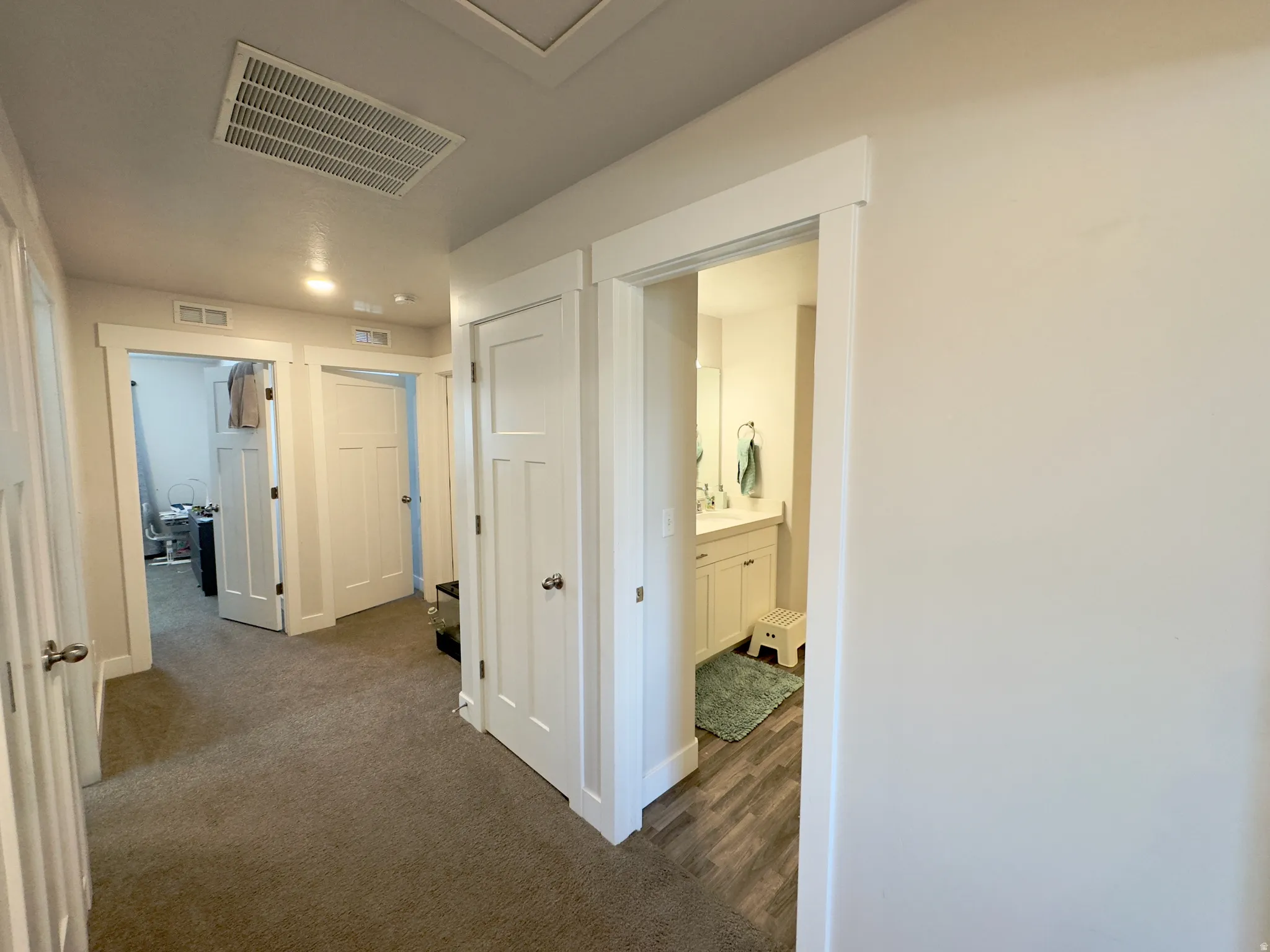 Hallway with carpeted flooring, leading to multiple rooms with white doors and white trim
