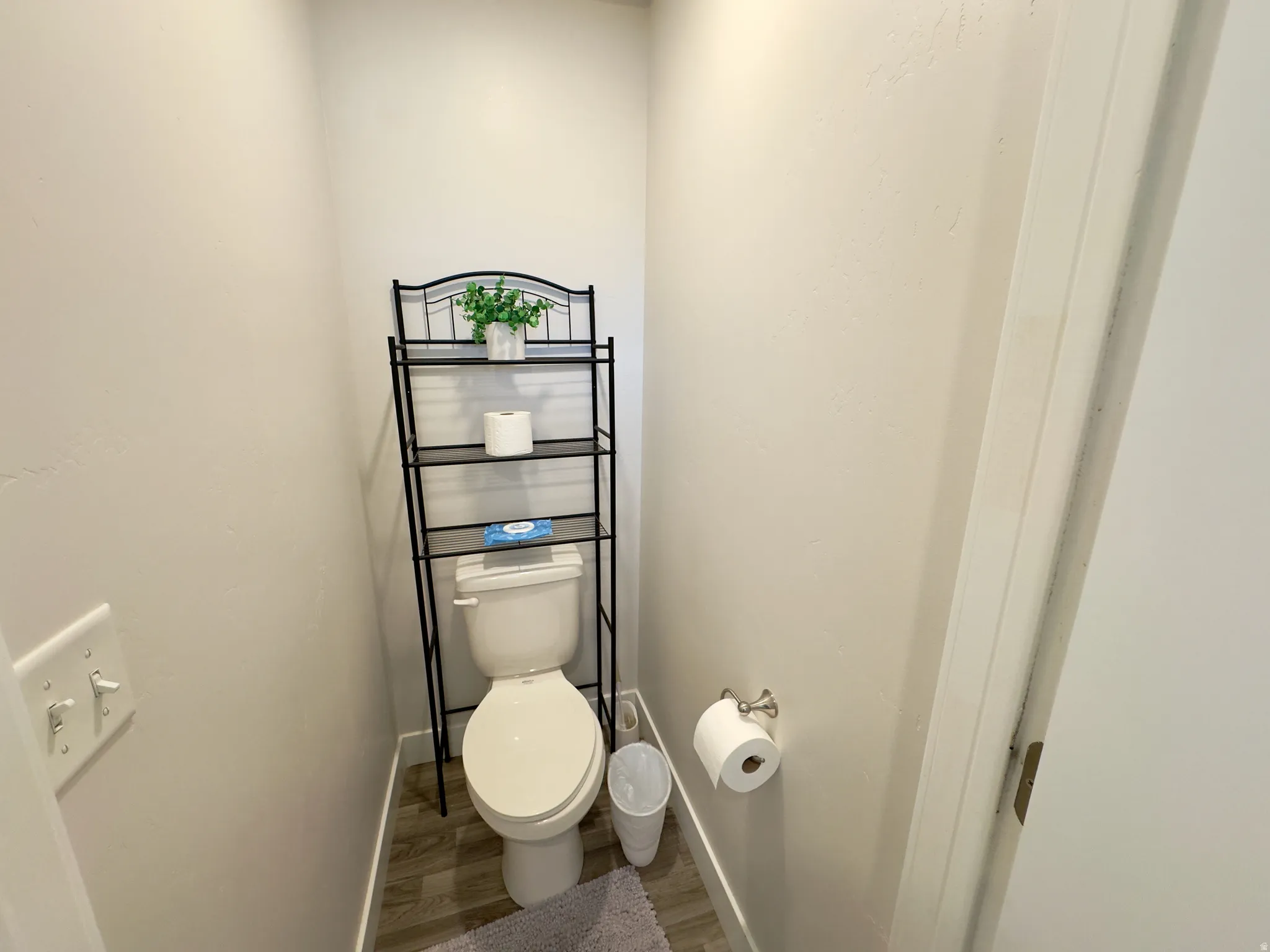 Powder room featuring light neutral wall paint, wood-finish flooring, and a white toilet