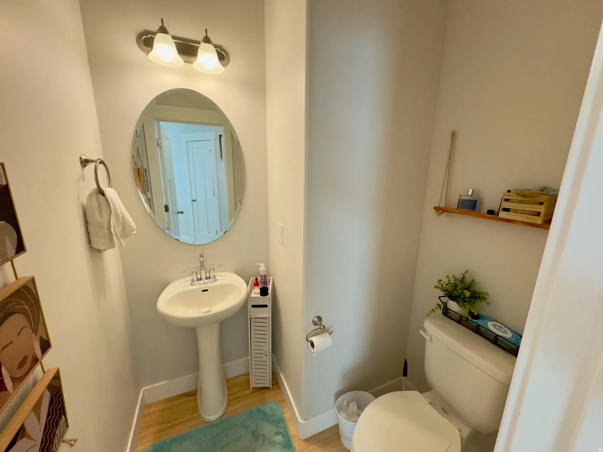 Pedestal sink with a chrome faucet, oval mirror, and overhead vanity lighting