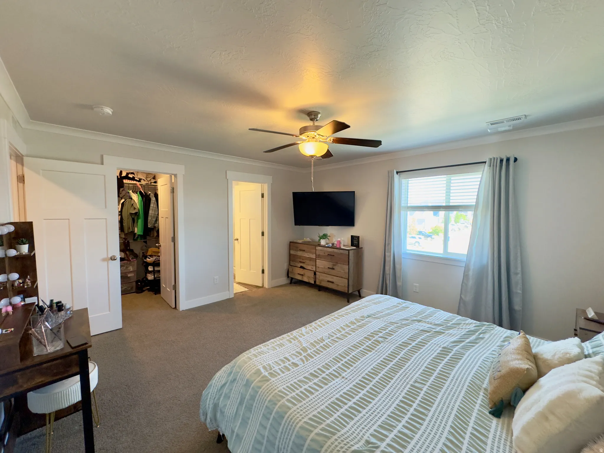 Carpeted bedroom with a ceiling fan light fixture, natural light from a window with blinds, and crown molding