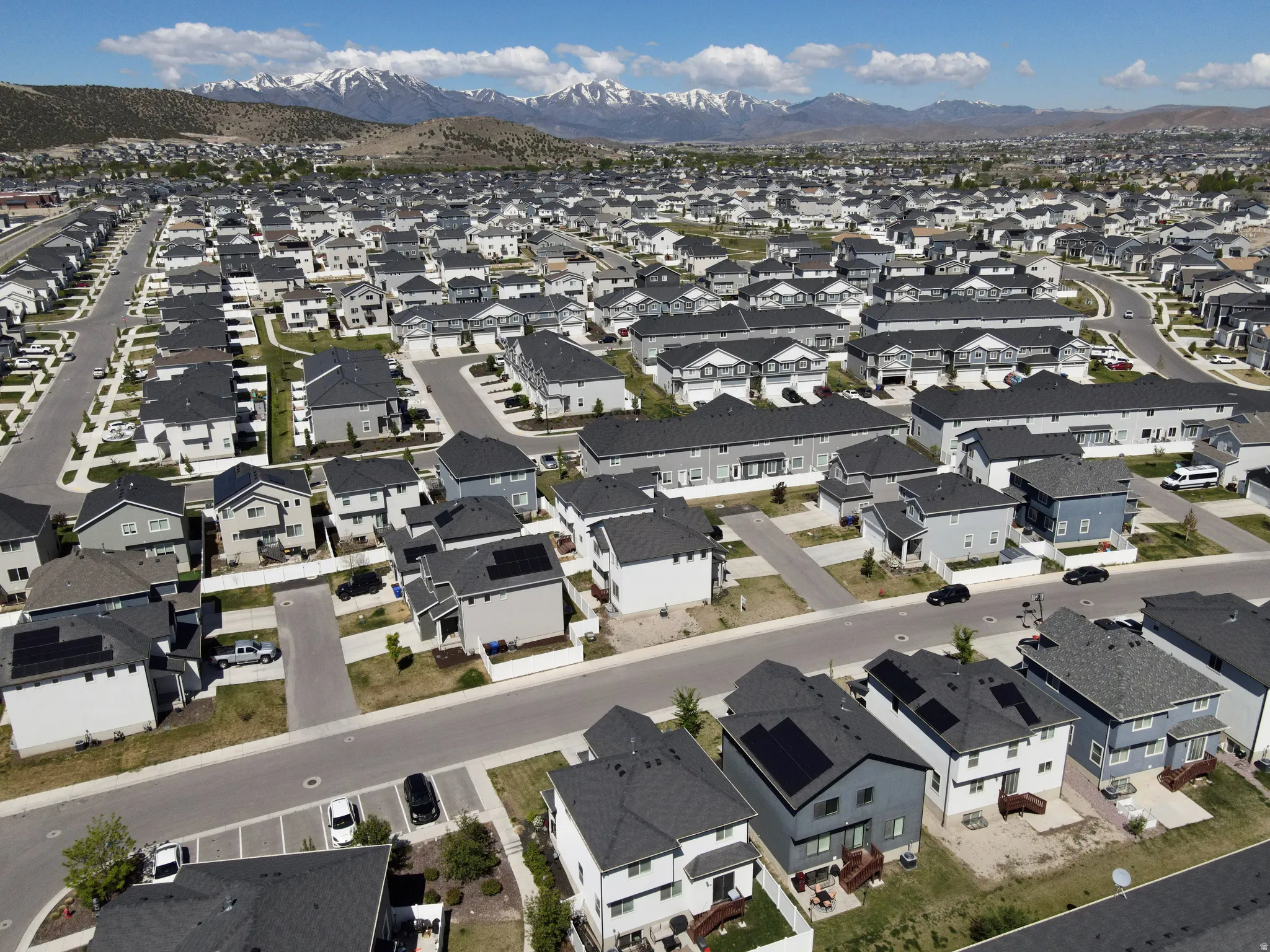 Expansive residential development featuring a cohesive neighborhood design with numerous detached homes and townhomes, a network of paved streets, and a backdrop of snow-capped mountains
