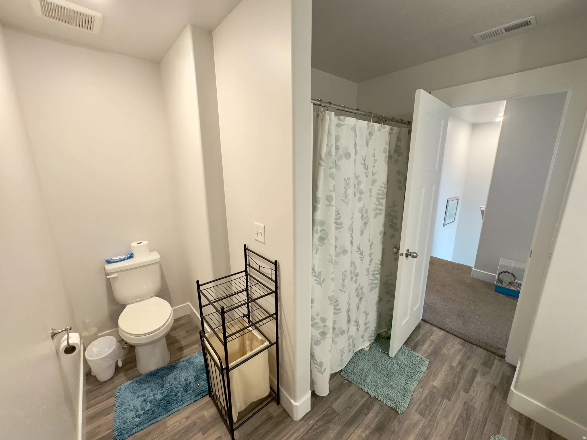 Bathroom featuring wood-finish flooring, a white toilet, and a shower area