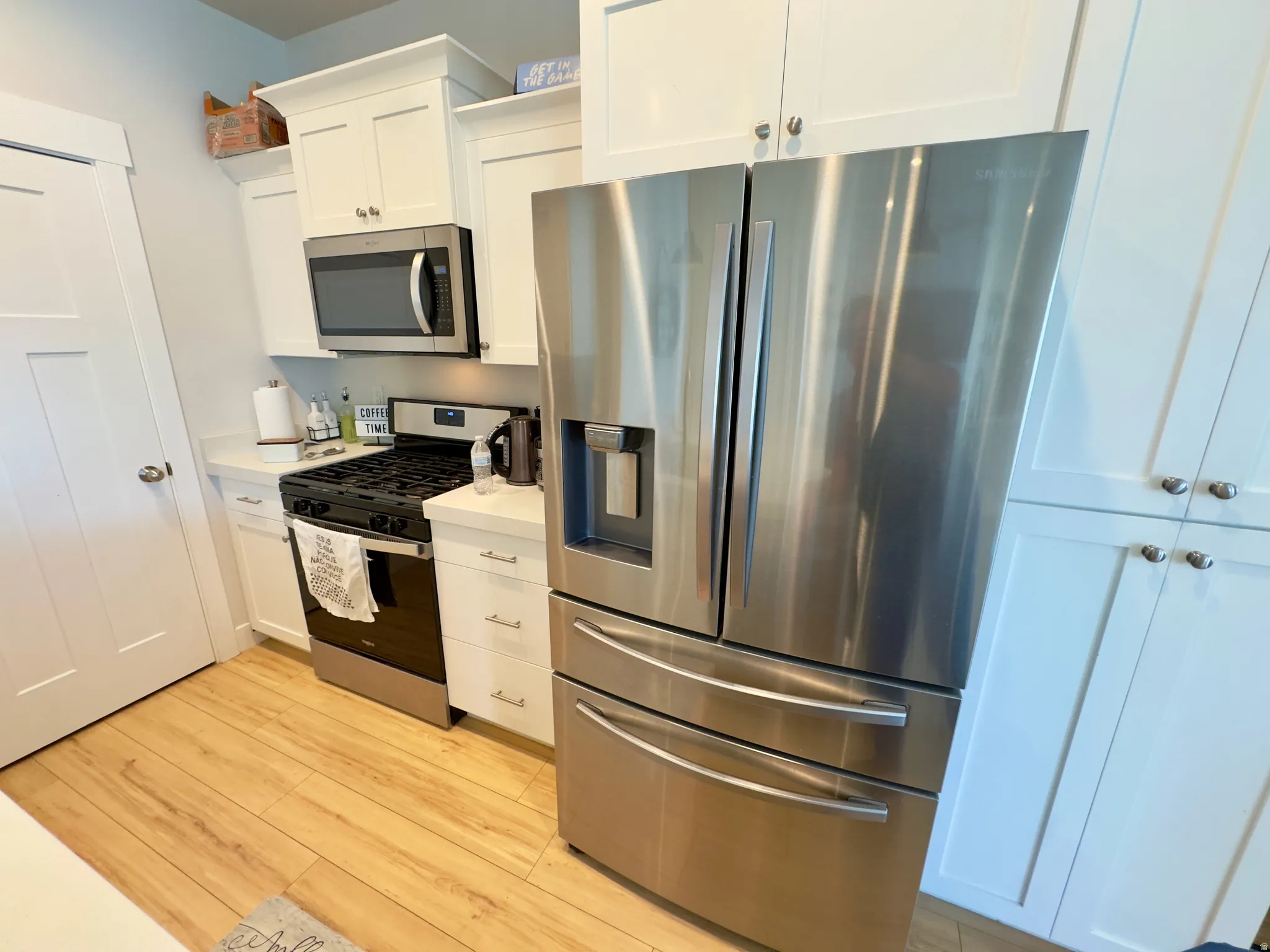Kitchen featuring white shaker-style cabinetry, stainless steel appliances, a gas range, light wood-finish flooring, and light-toned countertops