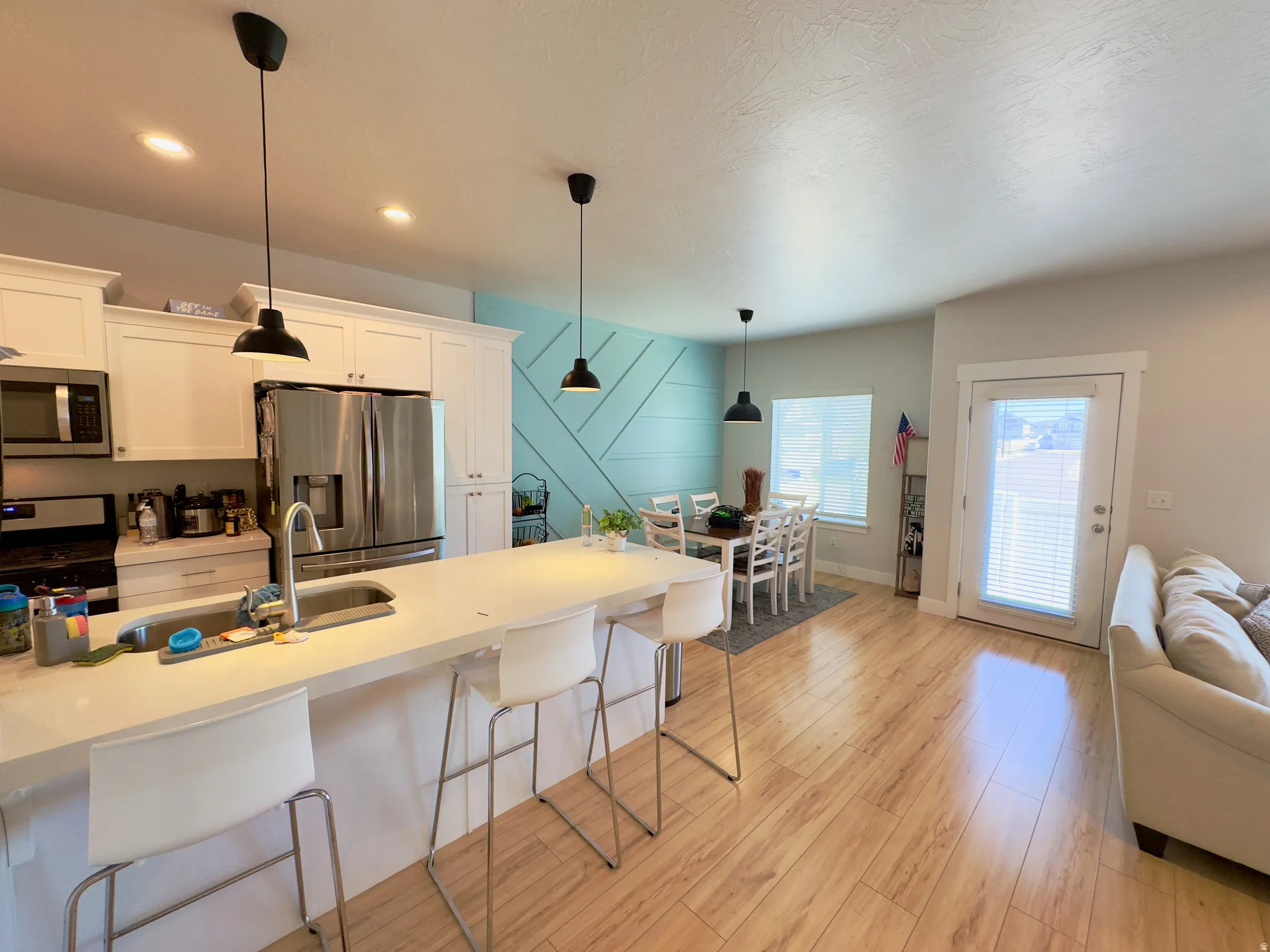 Open-concept kitchen and dining area featuring a spacious island with an undermount sink, white cabinetry, stainless steel appliances, and wood-finish flooring