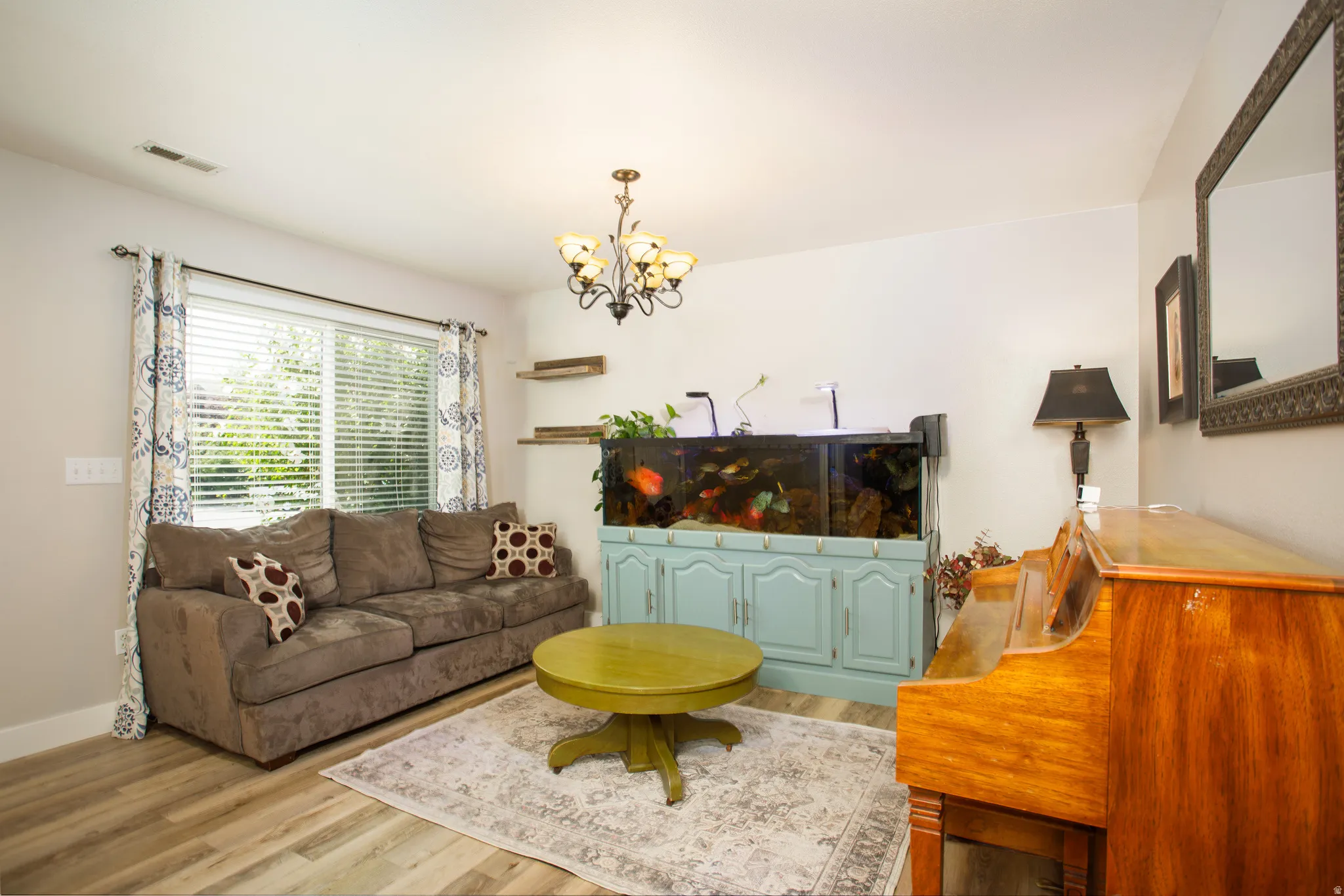 Spacious living area featuring wood-finish flooring, a large window with blinds, and a decorative chandelier