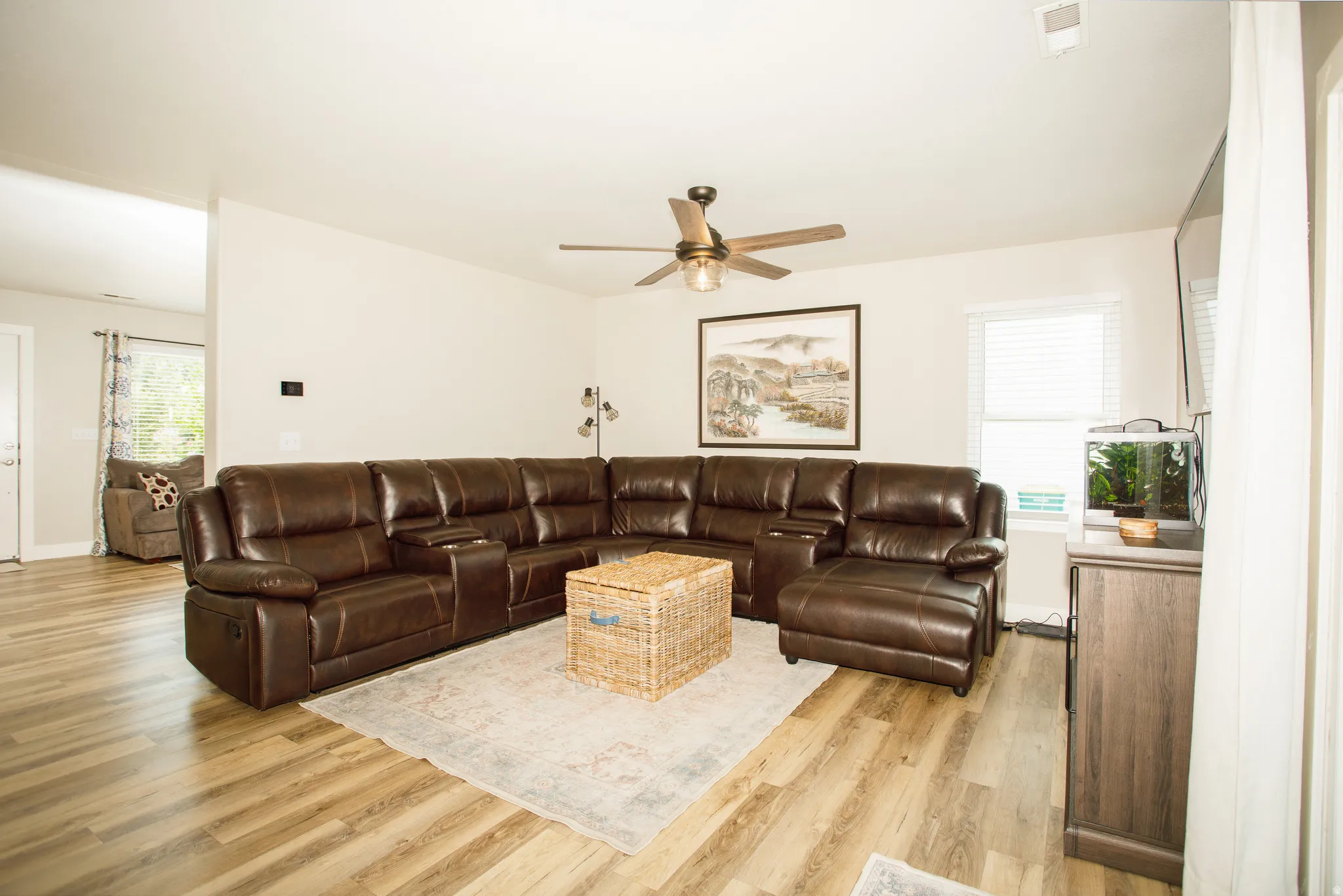 Spacious living area featuring wood-finish flooring, neutral wall tones, and a ceiling fan with light fixture