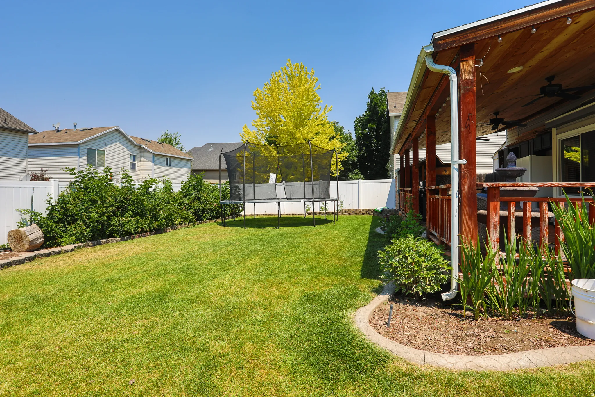 Expansive backyard featuring a manicured lawn, established shrubs, and a white privacy fence