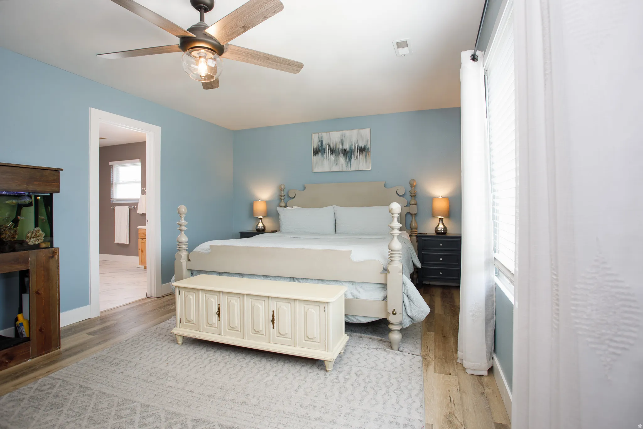 Spacious room featuring wood-finish flooring, a ceiling fan with integrated lighting, and a large window with blinds