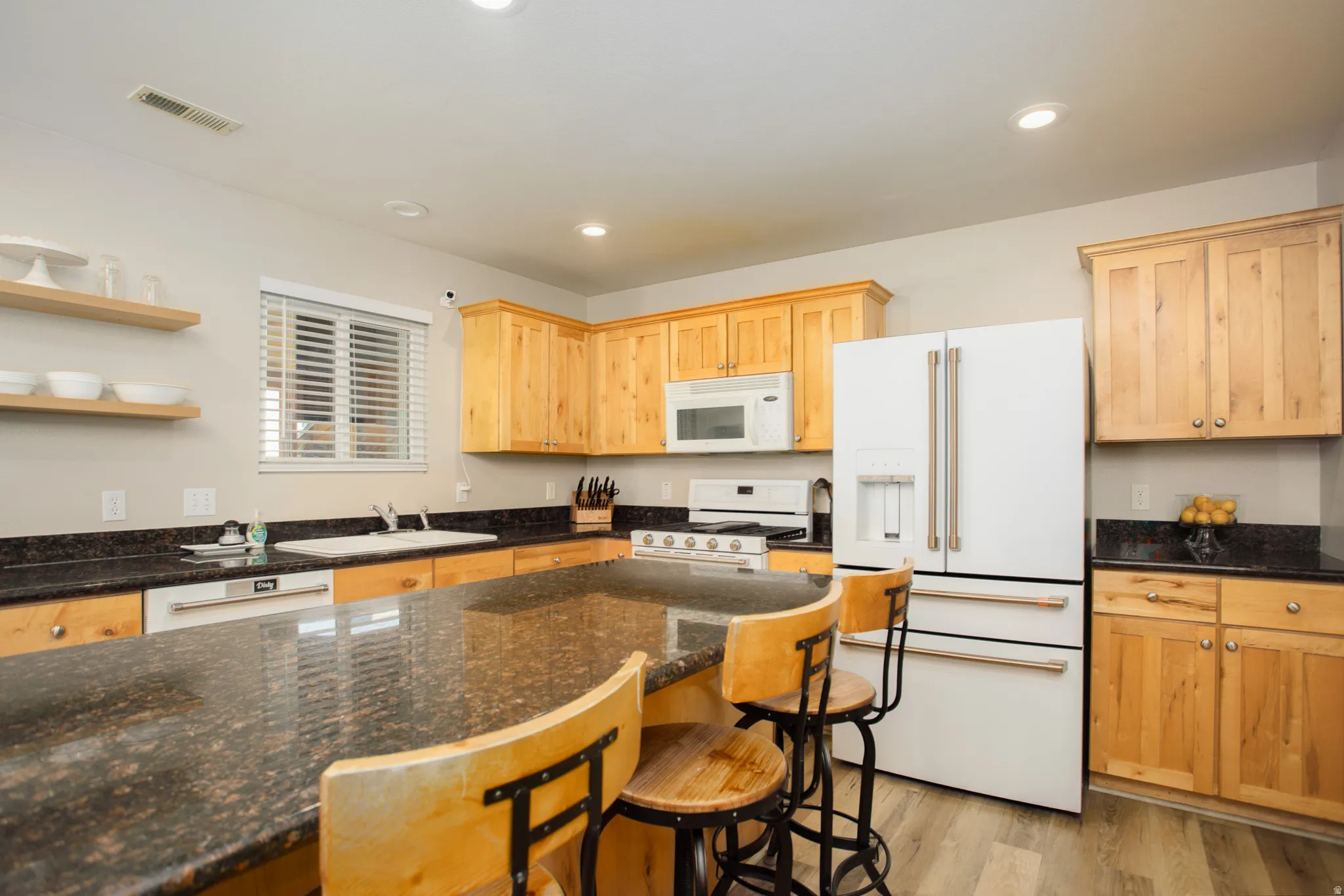 Kitchen featuring a spacious island with a dark stone countertop, wood-finish flooring, natural wood cabinetry, white appliances, and recessed lighting