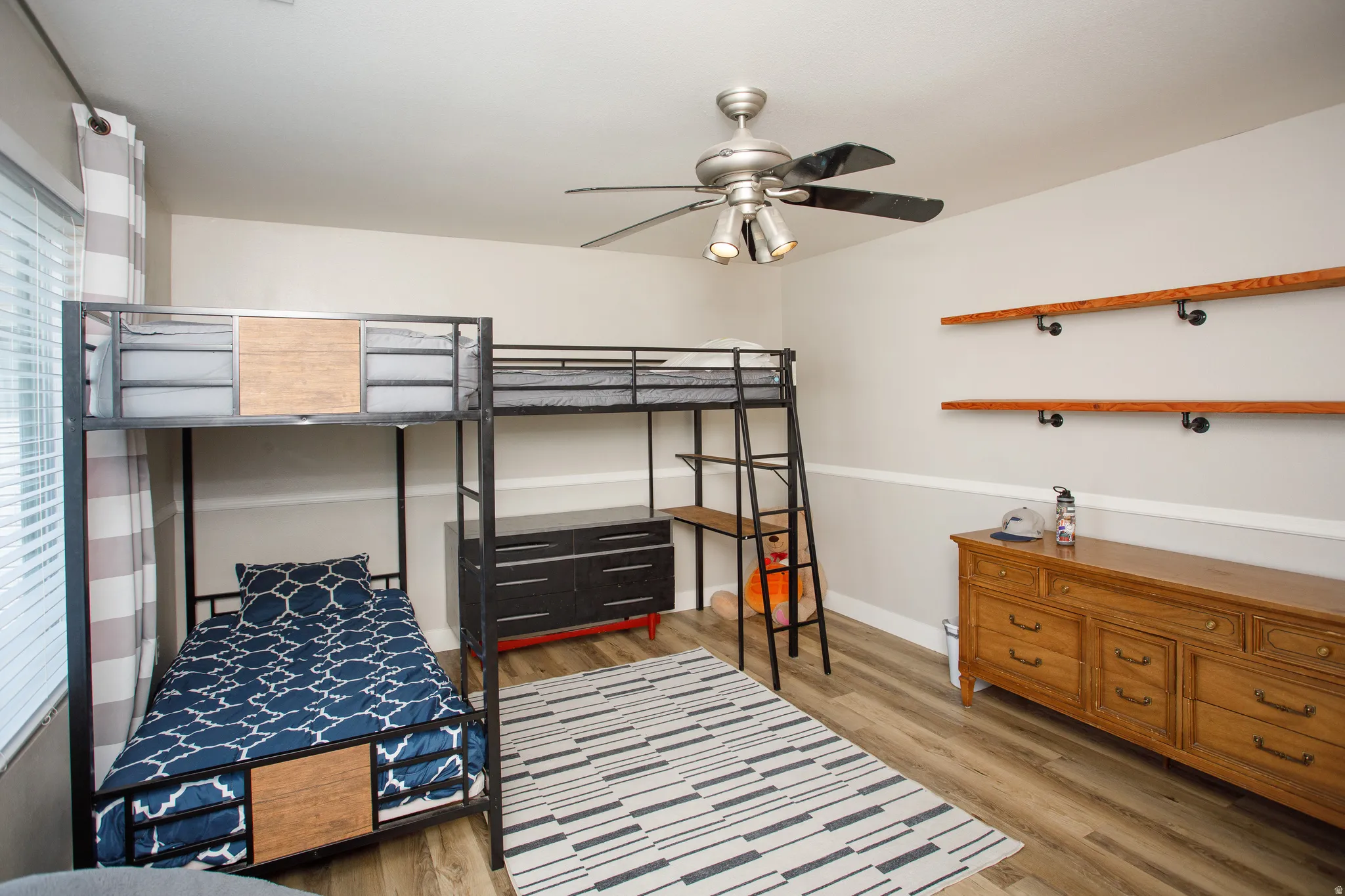 Room featuring light wood-finish flooring, a ceiling fan with integrated lighting, and horizontal wall shelving