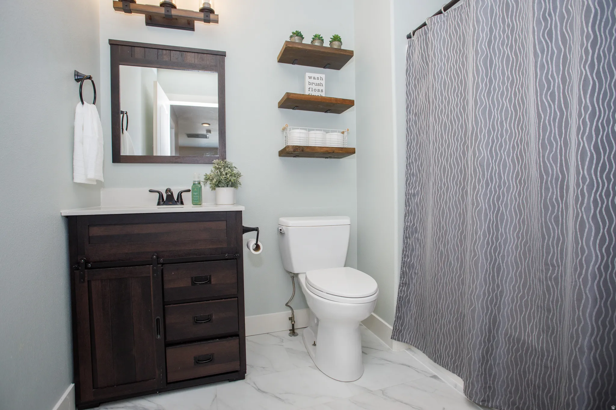 Bathroom featuring a dark wood-finish vanity with a white countertop and rectangular sink, complemented by a matching framed mirror and overhead light fixture