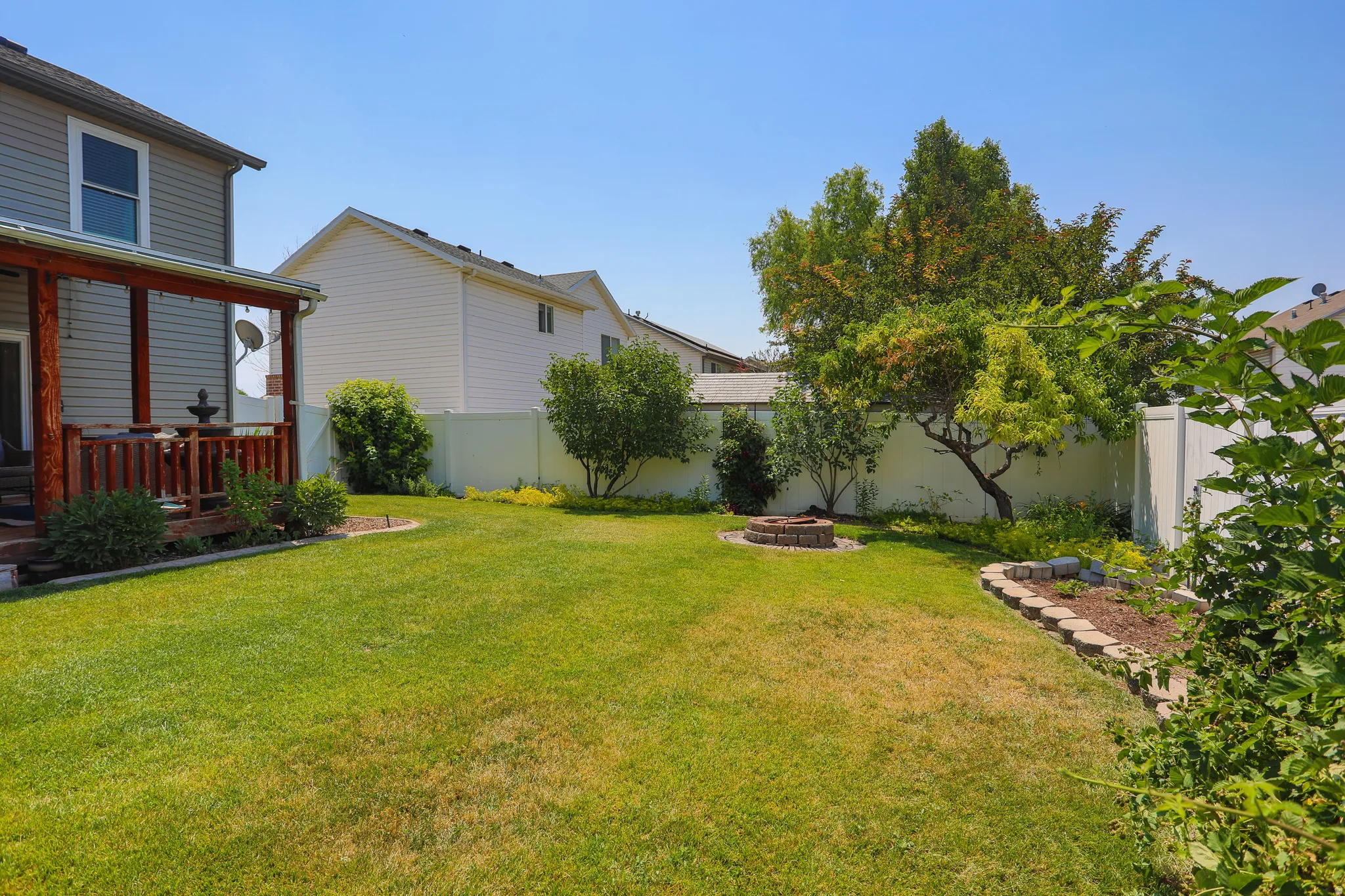 Expansive lawn featuring a built-in fire pit, stone-edged garden bed, mature trees, and privacy fencing