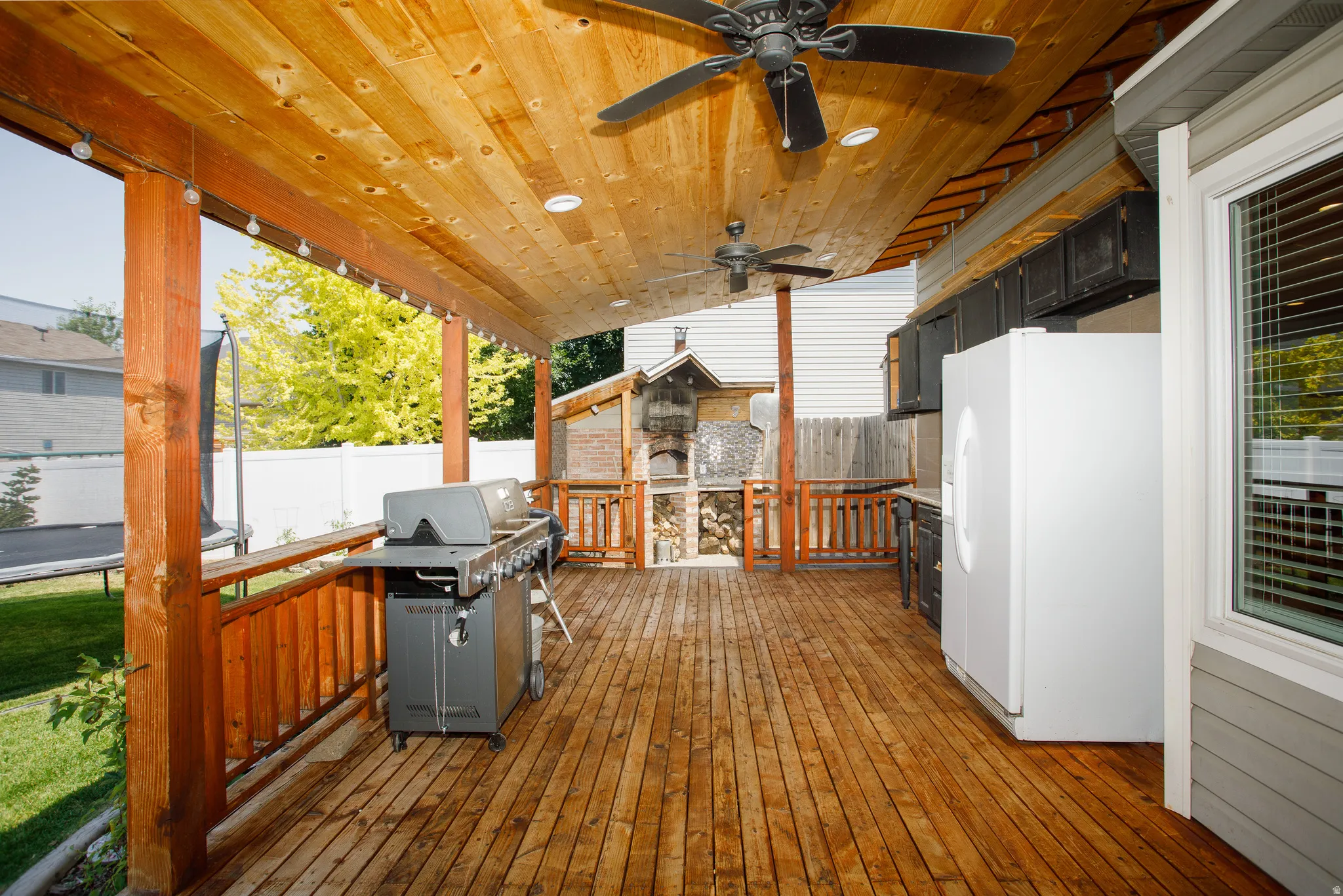 Expansive covered deck featuring wood-finish flooring, a wood-plank ceiling with recessed lighting and ceiling fans, and built-in cabinetry