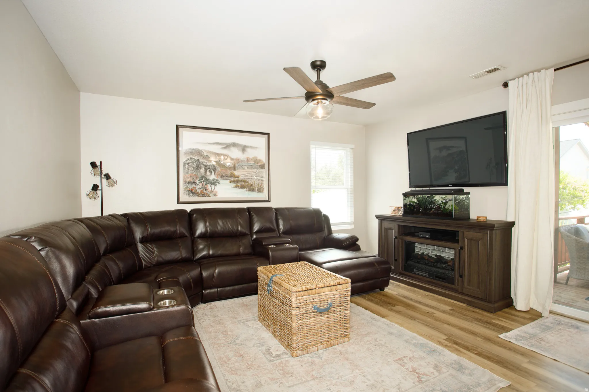 Spacious living area featuring wood-finish flooring, a ceiling fan with integrated lighting, and a built-in media console with an electric fireplace insert