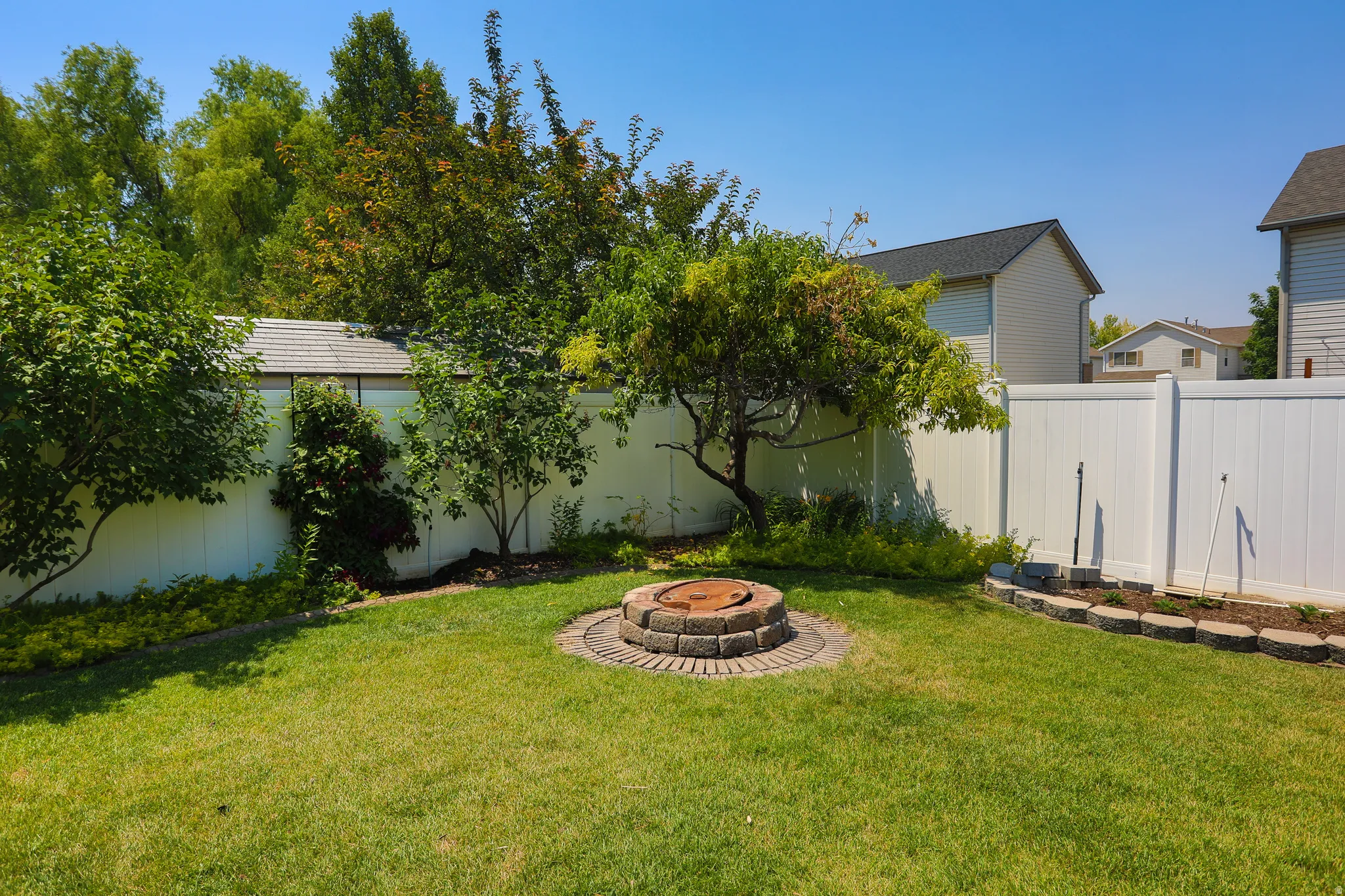 Expansive backyard featuring a stone-ringed fire pit, manicured lawn, and mature trees