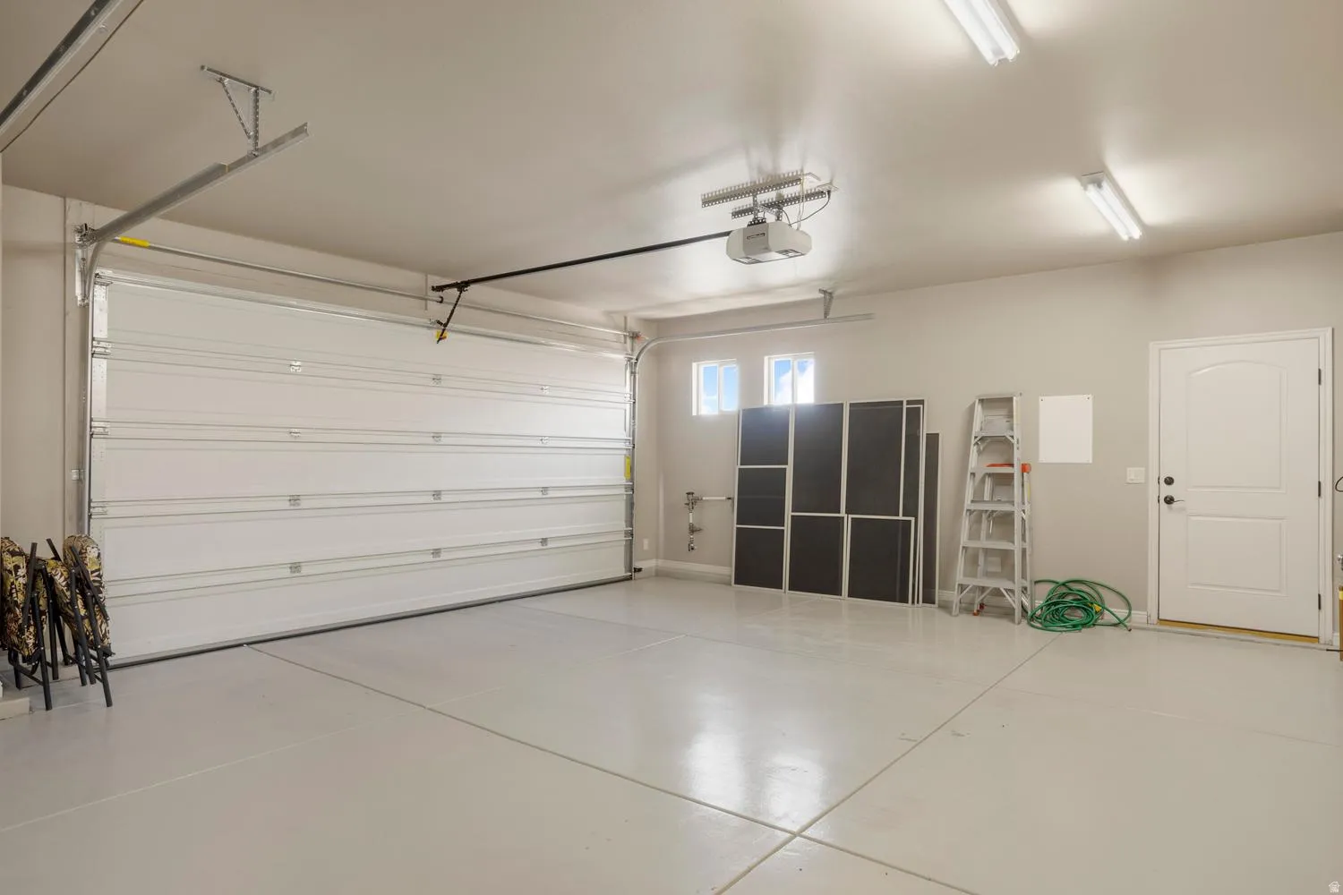 Spacious garage featuring a roll-up garage door, painted concrete flooring, an arched panel door, and overhead fluorescent lighting