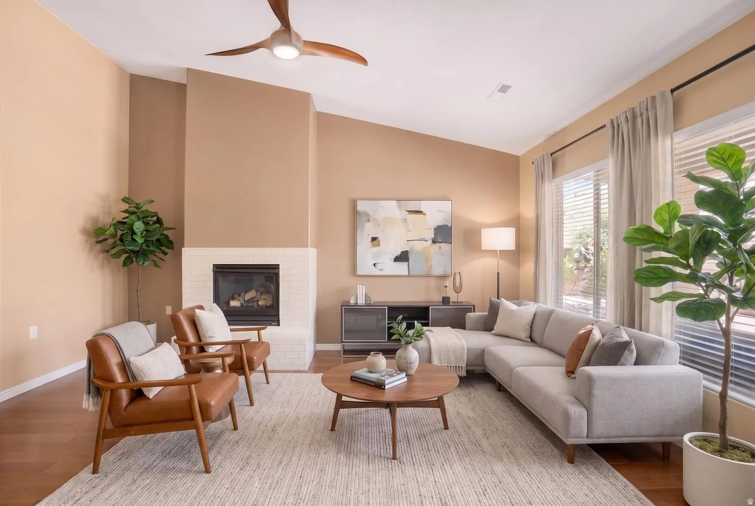 Vaulted ceiling with a contemporary ceiling fan, wood-finish flooring, a fireplace with a white tile surround, and large windows with blinds