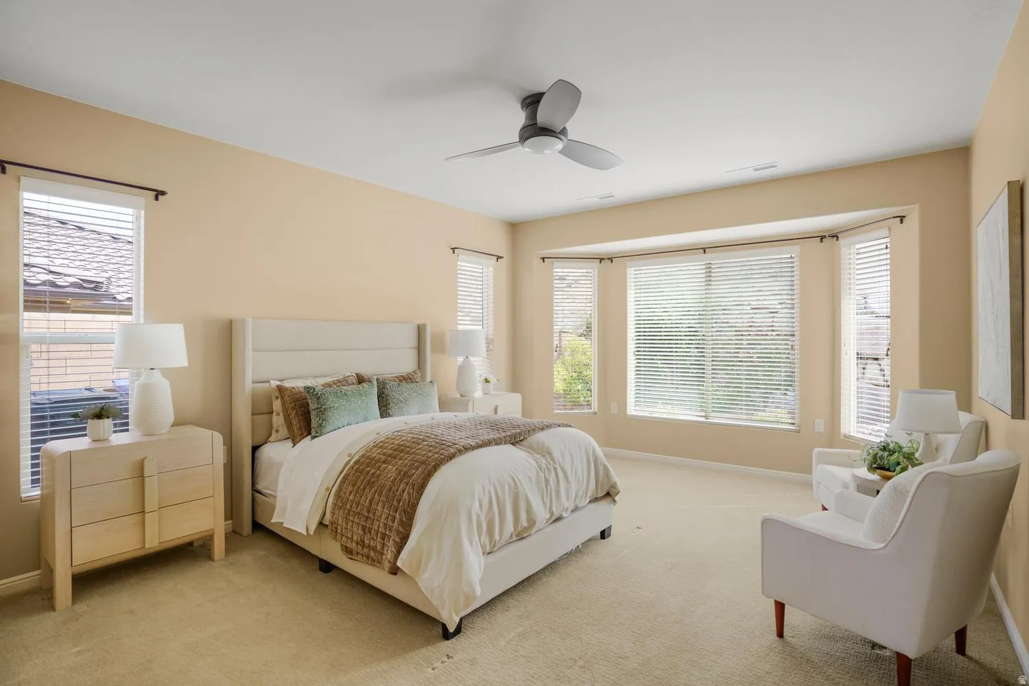 Spacious room featuring a ceiling fan, bay window, multiple windows, and carpet flooring