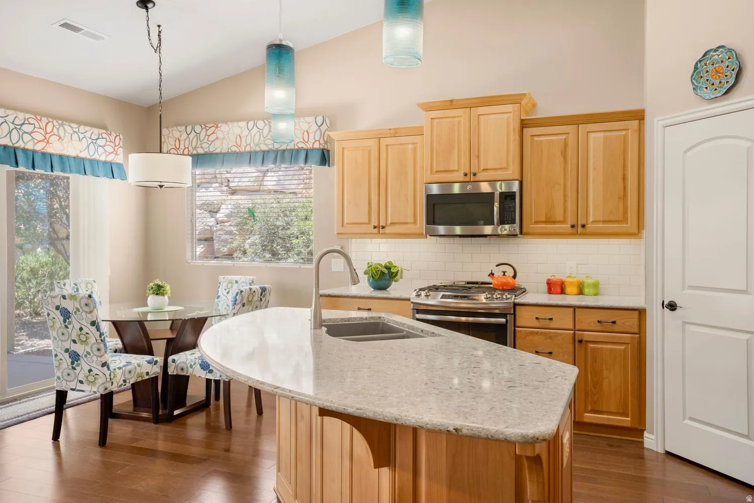 Kitchen featuring wood-finish flooring, light wood cabinetry, stainless steel appliances, and a tile backsplash