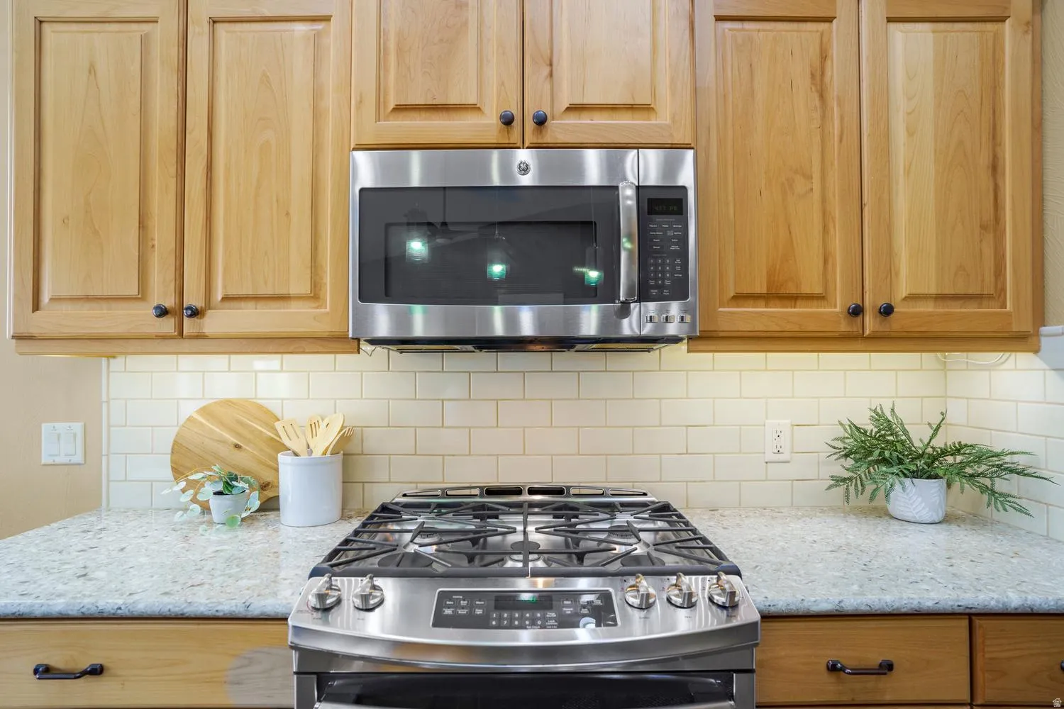 Stainless steel range with a built-in microwave, light wood cabinetry, subway tile backsplash, and light-colored countertops