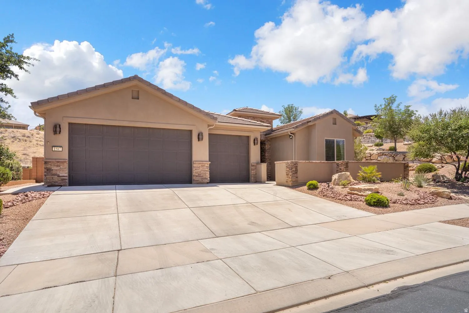 Stucco exterior with stone accents, concrete driveway, two garage doors, and xeriscaped front yard