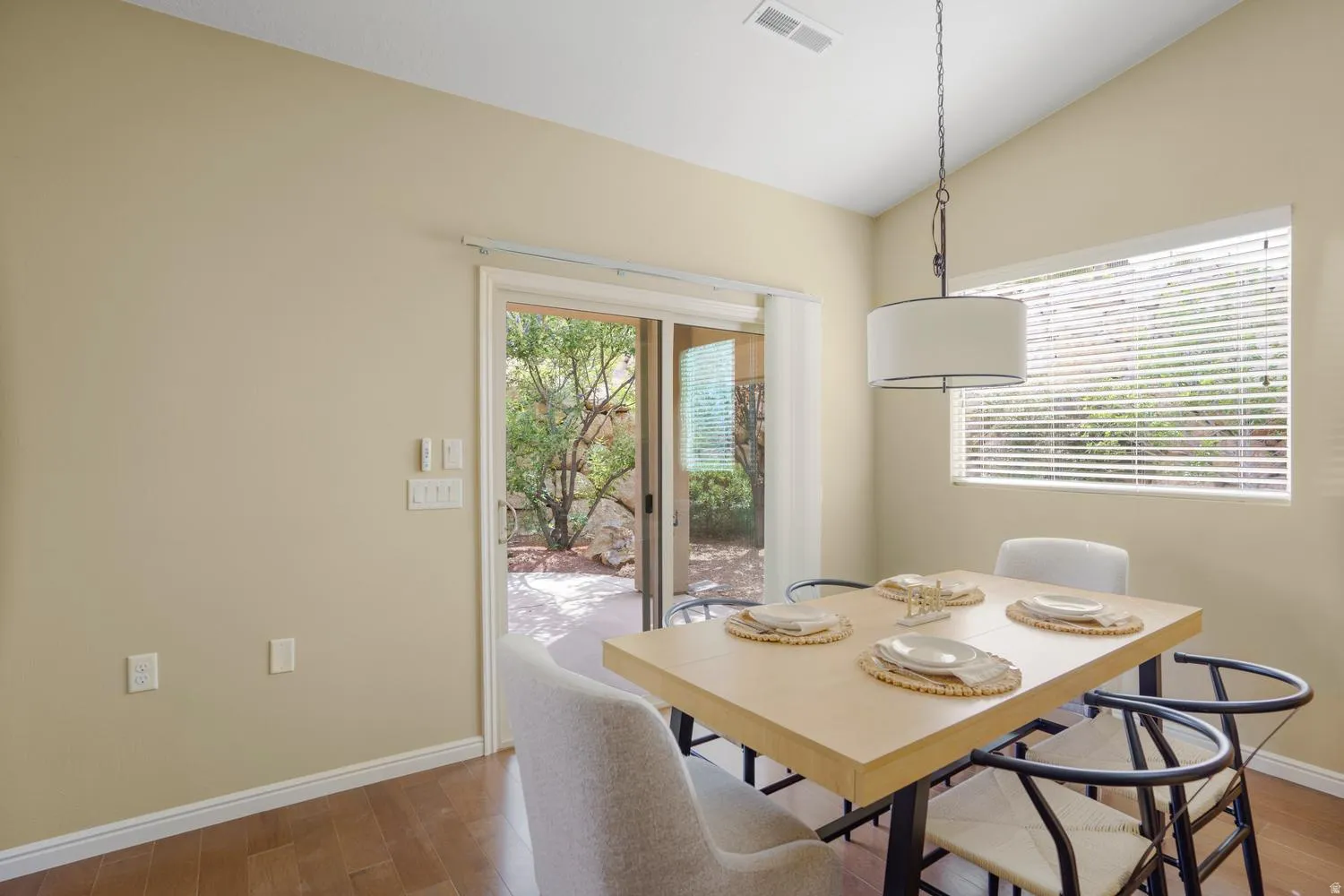 Wood-finish flooring, vaulted ceiling, drum pendant light fixture, sliding glass door, and a horizontal window with blinds