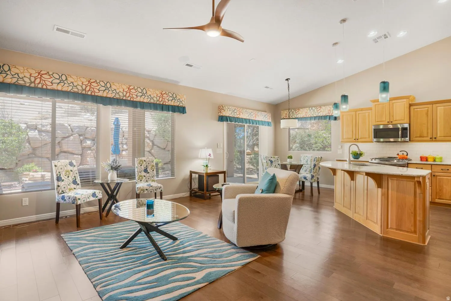 Open-concept living space featuring wood-finish flooring, vaulted ceilings, and large windows with custom valances