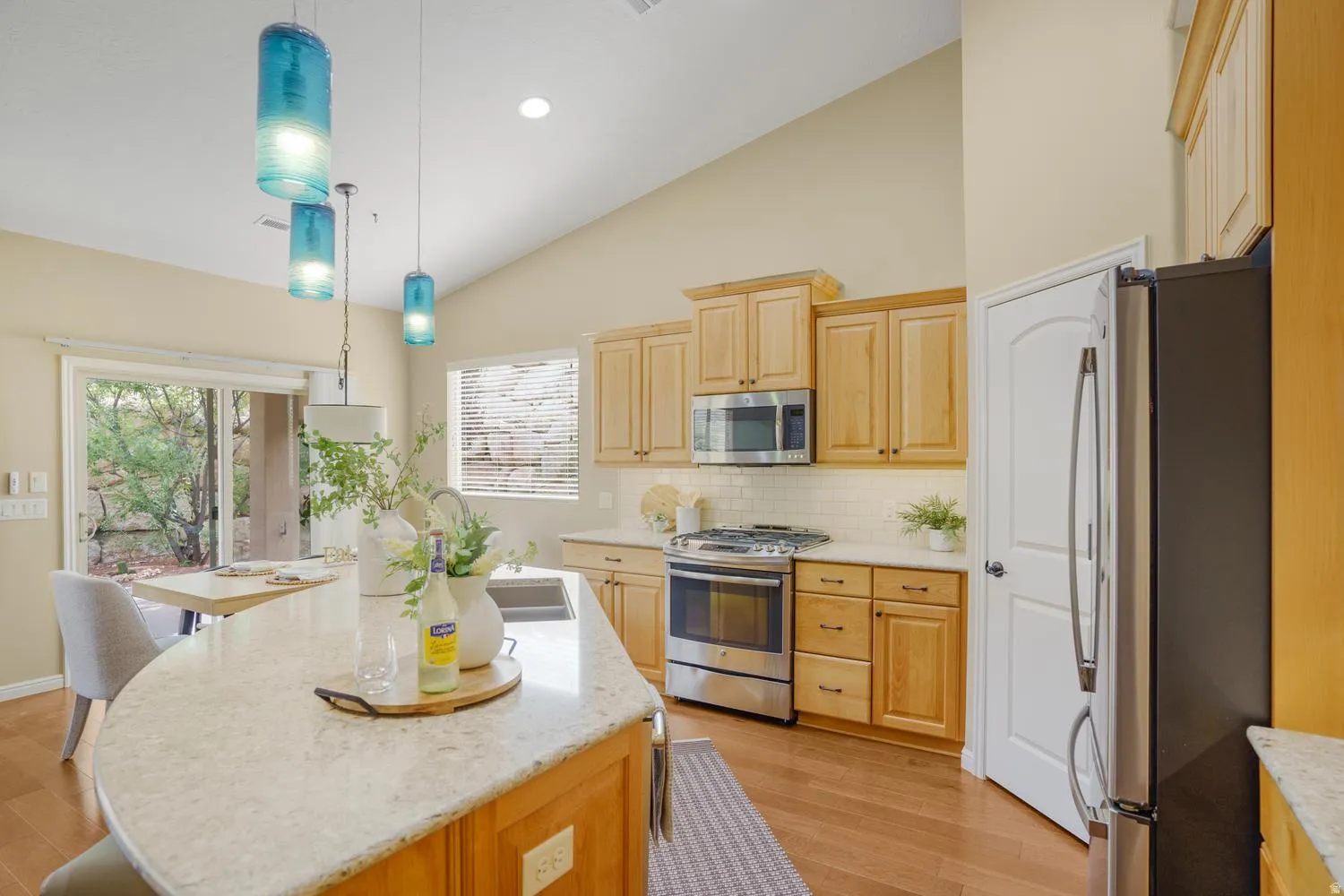 Kitchen with vaulted ceiling, wood-finish flooring, stainless steel appliances, and a curved island with an undermount sink