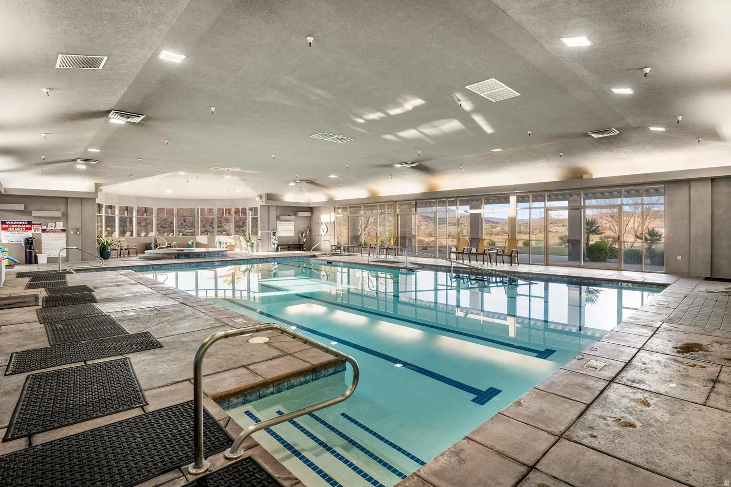 Indoor swimming pool featuring a built-in spa, expansive window walls, and tiled pool deck