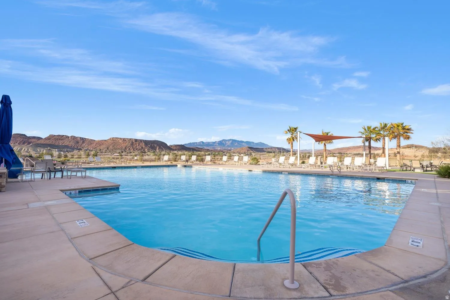 Expansive outdoor pool with a concrete surround, integrated pool steps, and a metal handrail