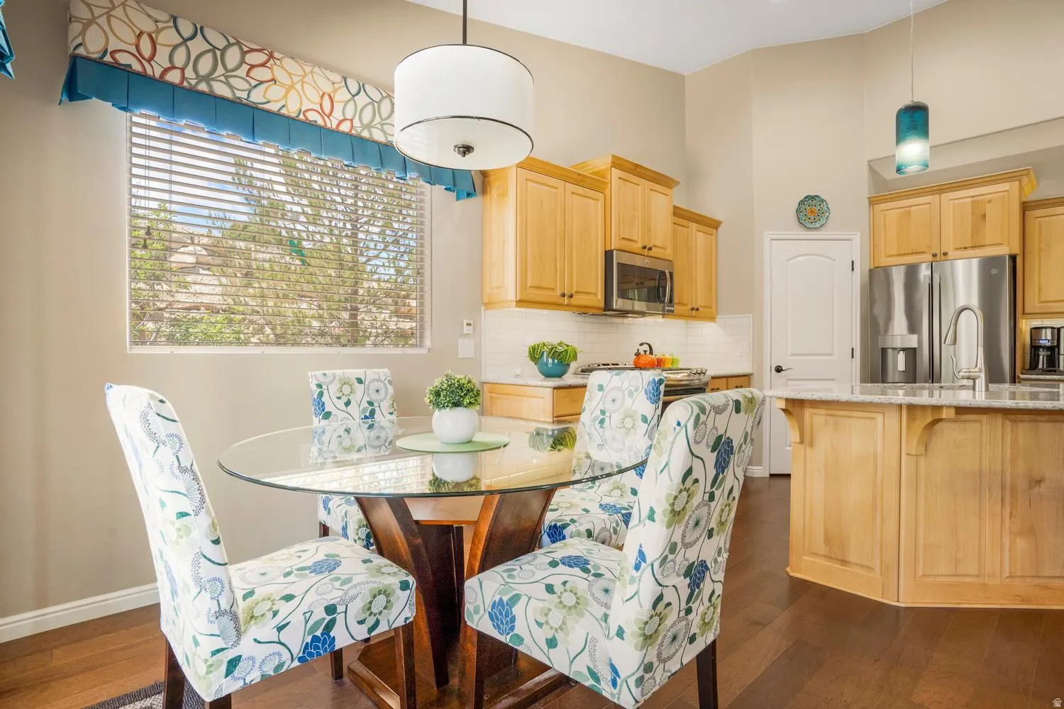 Open-concept kitchen and dining area featuring hardwood flooring, light wood cabinetry, stainless steel appliances, and a kitchen island with seating