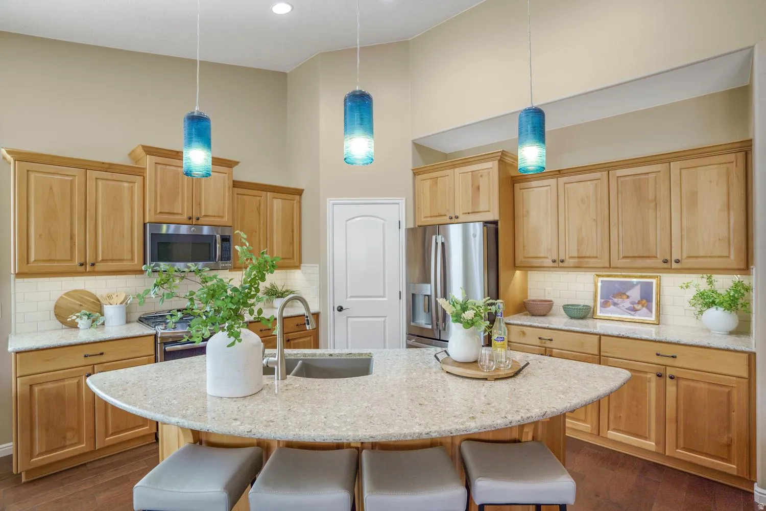 Kitchen featuring wood cabinetry, stainless steel appliances, a tile backsplash, light-toned countertops, and a central island with an undermount sink