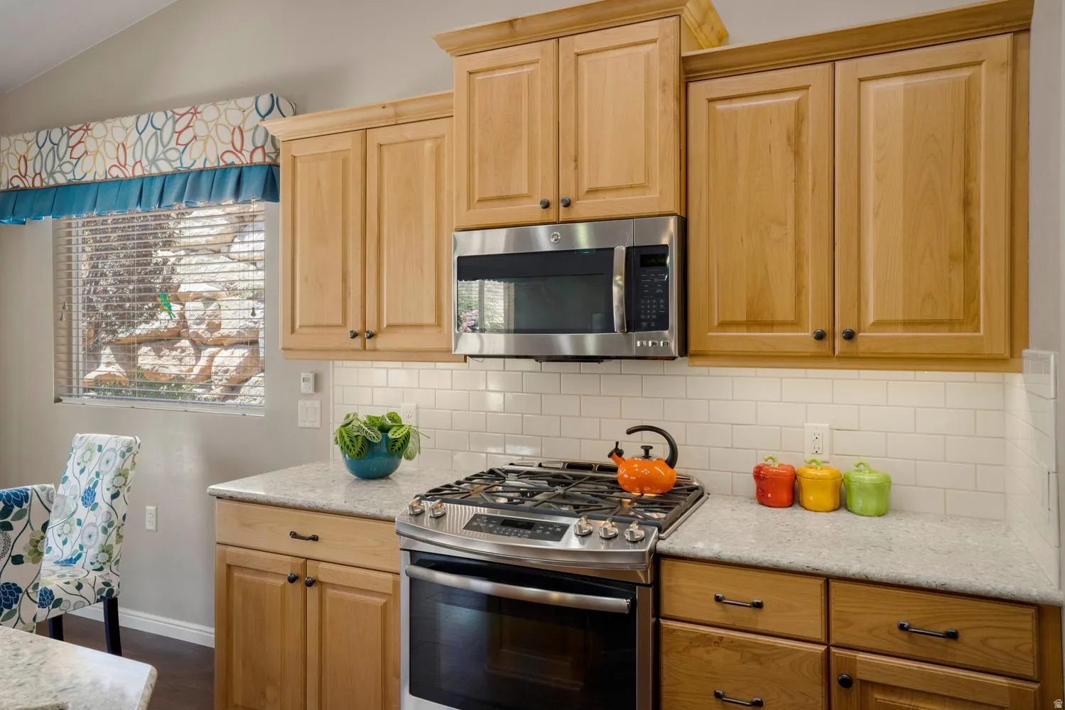 Kitchen featuring light wood cabinetry, stainless steel microwave, stainless steel range, light-toned countertops, and a white subway tile backsplash