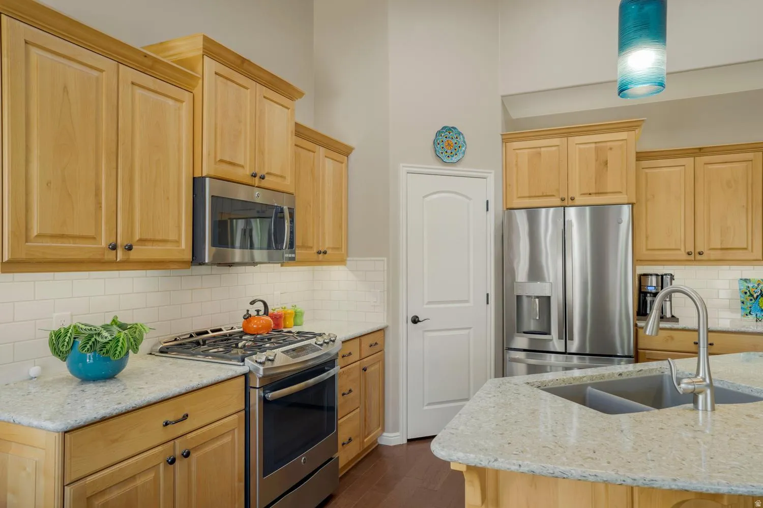 Kitchen featuring light wood cabinetry, stainless steel appliances, light speckled countertops, subway tile backsplash, and a double basin sink with a gooseneck faucet