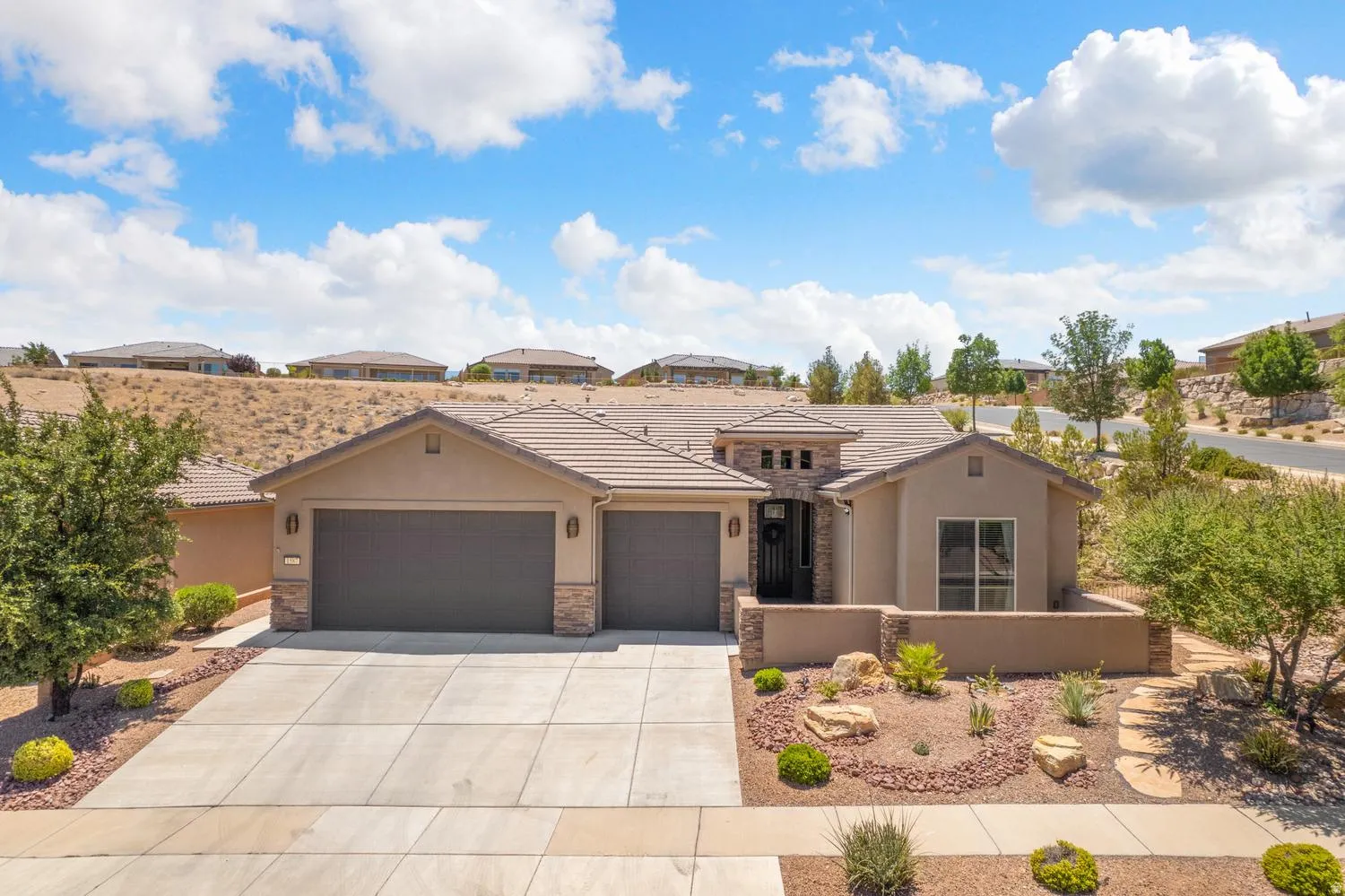 Contemporary stucco and stone-accented home featuring a concrete driveway, two-car garage, tile roof, and desert-style landscaping