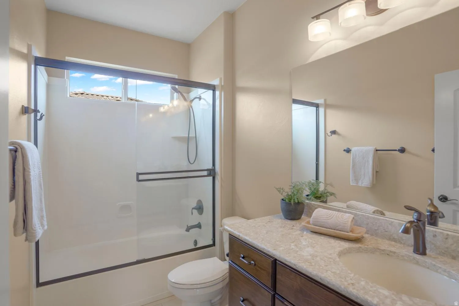 Tub/shower combination with a sliding glass enclosure, transom window, vanity with a light-colored countertop, built-in sink, and a large wall-mounted mirror