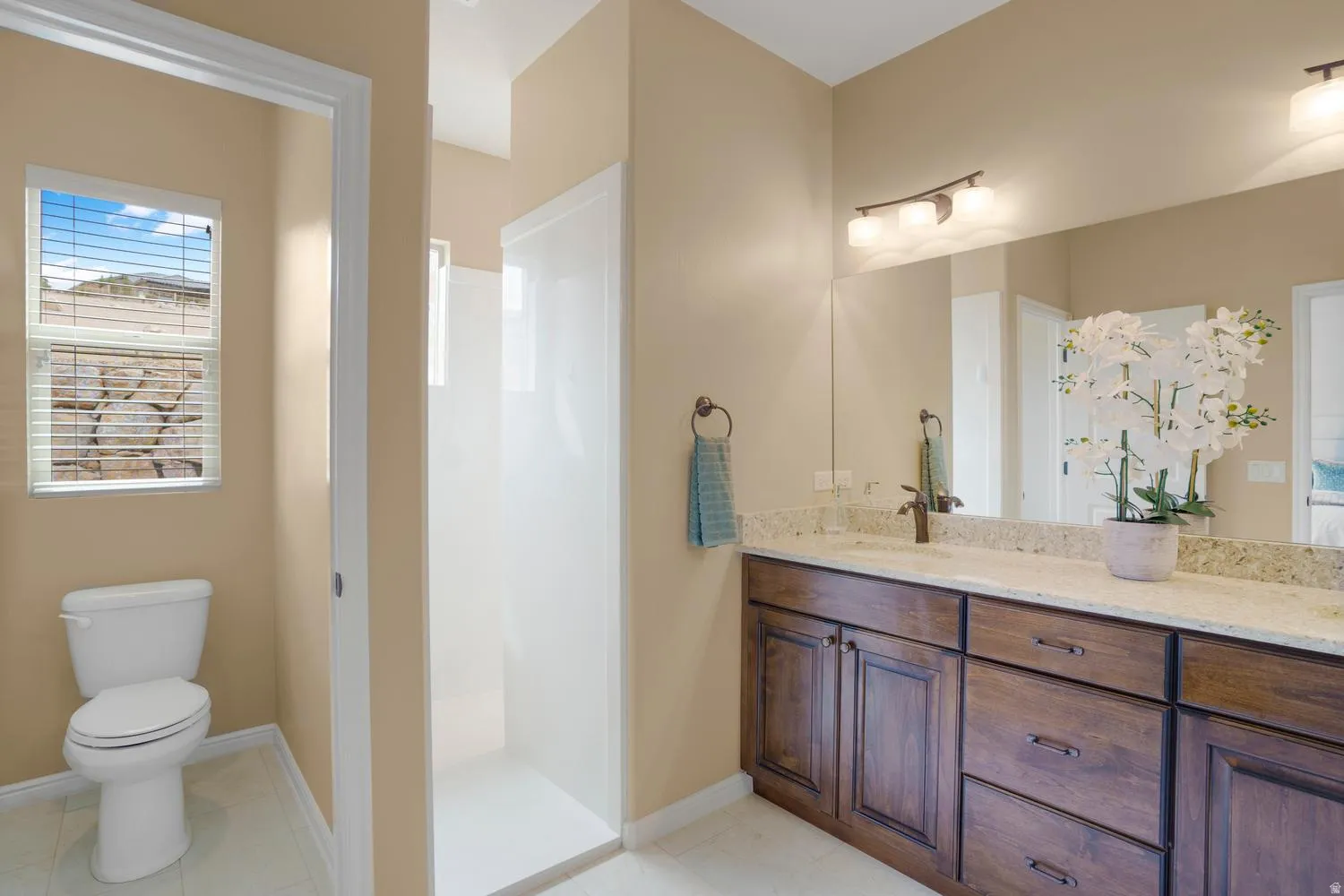 Dual vanity with a light-toned countertop, wood-finish cabinetry, and a large mirror
