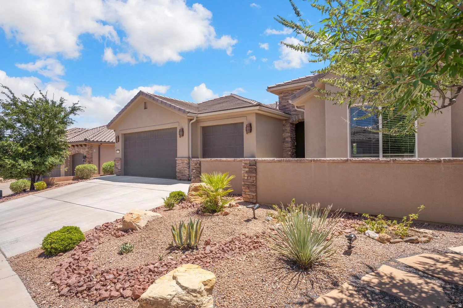 Stucco exterior with stone accents, an attached two-car garage, concrete driveway, and desert landscaping